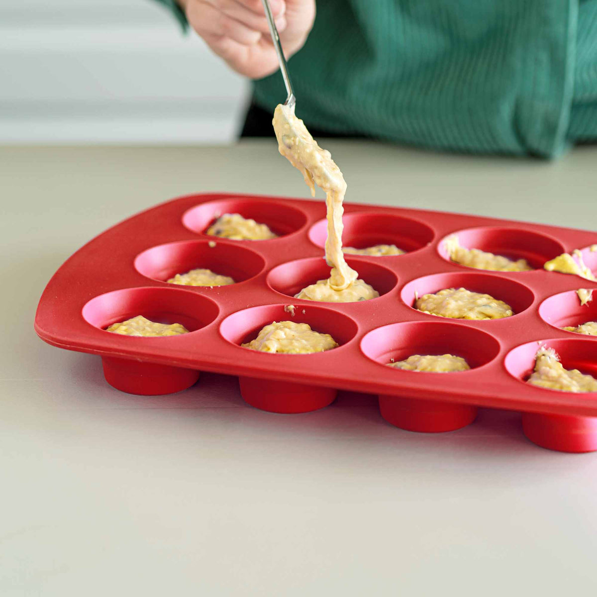 Silikoniseen muffinsivuokaan annostellaan taikinaa valkoisen keittiöntason päällä.