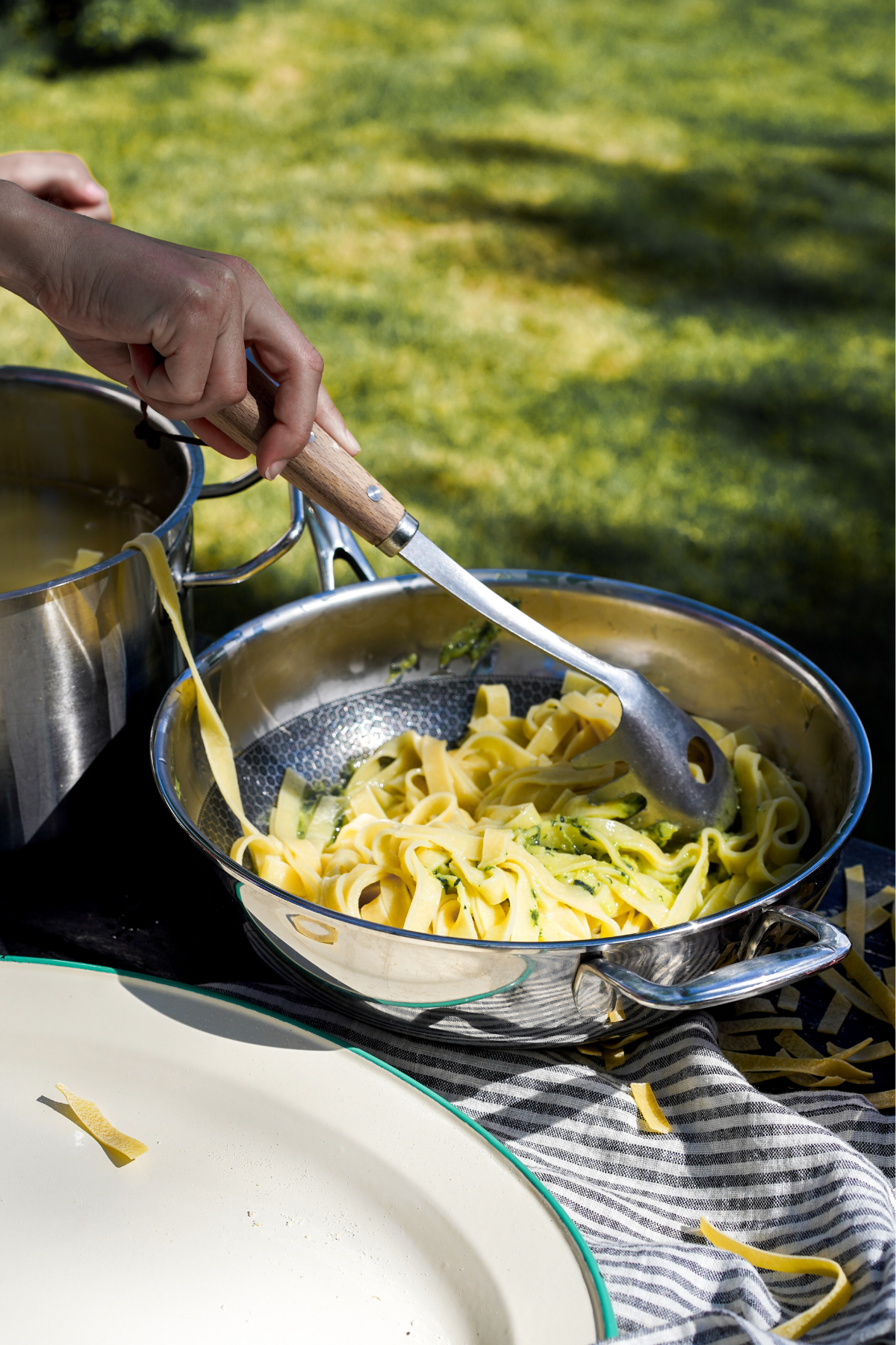 Ruostumattomasta teräksestä valmistetulla pastakauhalla puukahvalla otetaan pastaa syvästä paistinpannusta.
