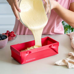 Silikoniseen leipävuokaan kaadetaan taikinaa vaaleassa keittiössä. Keittiön tasolla on vadelmia ja mustikoita. 