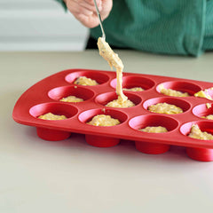 Silikoniseen muffinsivuokaan annostellaan taikinaa valkoisen keittiöntason päällä.